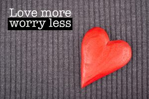 Inspirational motivation quote with phrase "Love more worry less", Red Wooden Heart on Knitted Background